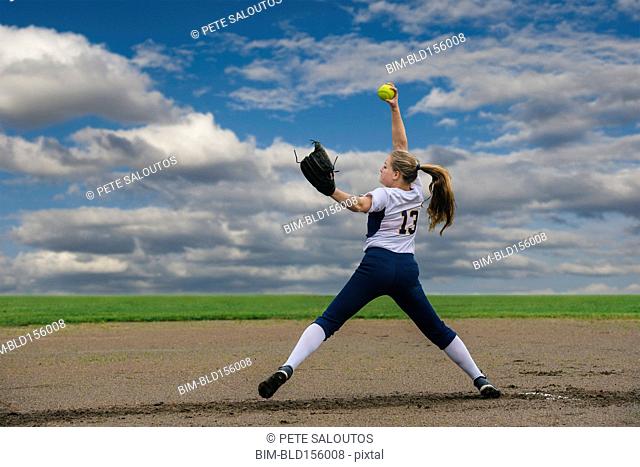 Caucasian softball player pitching ball in field