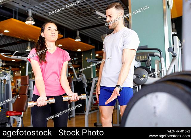Happy instructor motivating woman exercising with dumbbells at gym
