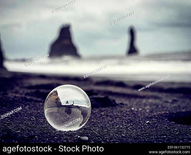 Cold sea water rolling on wet sand near rough stony cliffs on stormy day on Reynisfjara Black Beach in Iceland