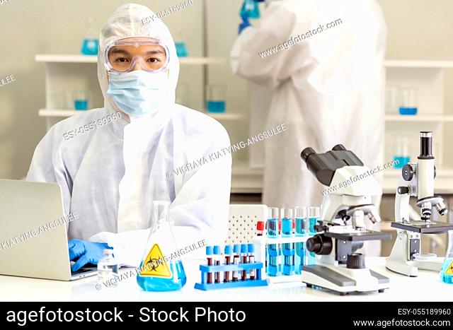 Scientists working in lab using laptop to research and develop vaccine for coronavirus covid-19 pandemic with his colleague in background