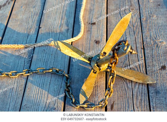 close-up anchor with chain in the rays of the morning sun lies on a wooden pier