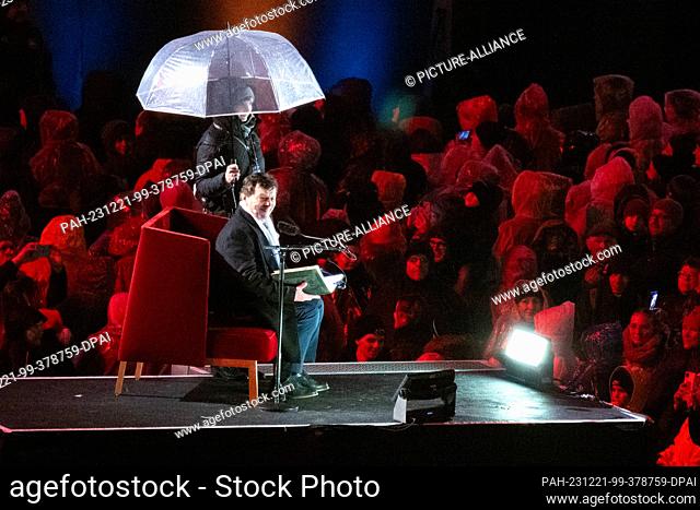 21 December 2023, Saxony, Dresden: Czech actor Pavel Travnicek sits on stage under an umbrella at the Advent concert in the Rudolf Harbig Stadium