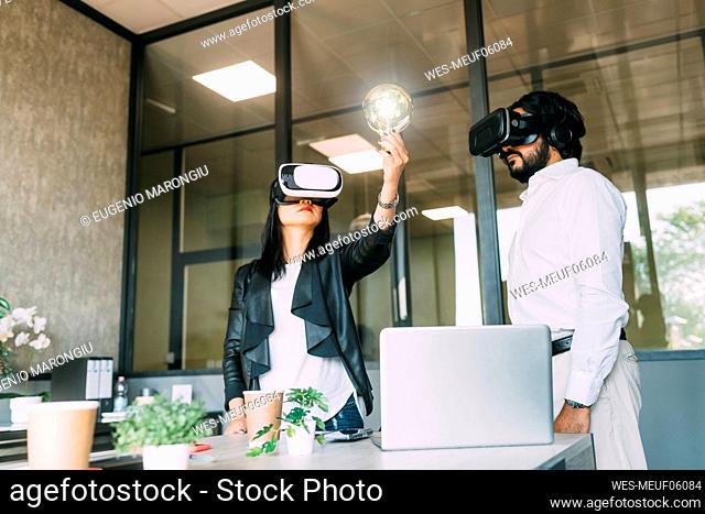 Businesswoman wearing VR glasses and examining light bulb by colleague