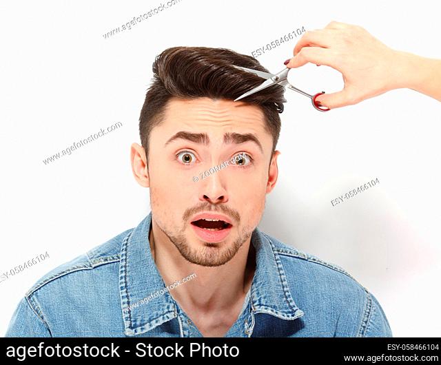 Portrait fo handsome man with black hair sitting in studio and having haircut. Frightened man looking at camera isolated on white background