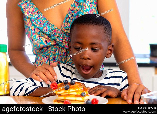 Midsection of multiracial mother standing by son with mouth open looking at pancakes and fruits