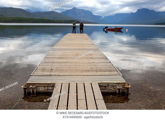 Photographers stand at the end of a long dock at Lake McDonald to capture images of sunset