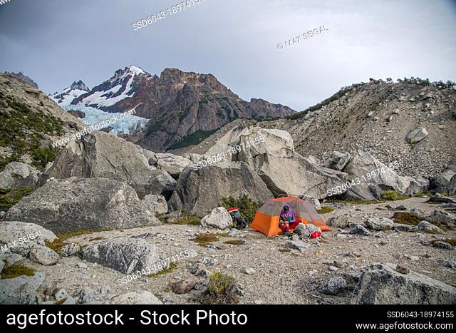 Hiker sitting in tent a dusk with Patagonia mountain range in background