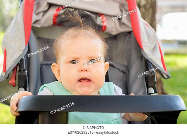 little girl sitting in a baby carriage on the street in summer