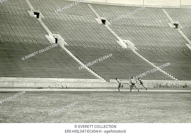 Relay racers practice baton handoff in an empty stadium, c. 1920. Unknown location (BSLOC-2018-4-200)
