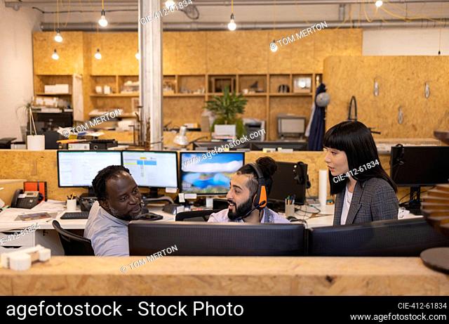 Business people talking at computers in open plan office