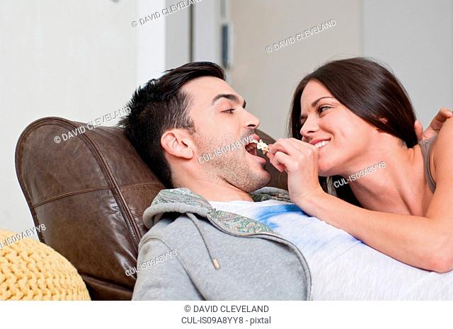 Young couple lying on sofa sharing popcorn