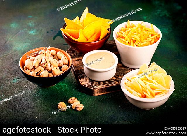 Assortment of unhealthy beer snacks: chips, nachos, pistachios, cheese in bowls, top view, copy space. Unhealthy eating concept