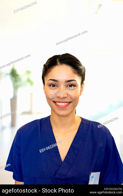 Vertical portrait of smiling biracial female healthcare worker in hospital corridor, with copy space