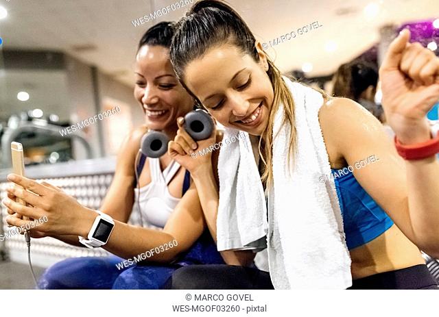 Two women having fun with their smartphone after work out in the gym