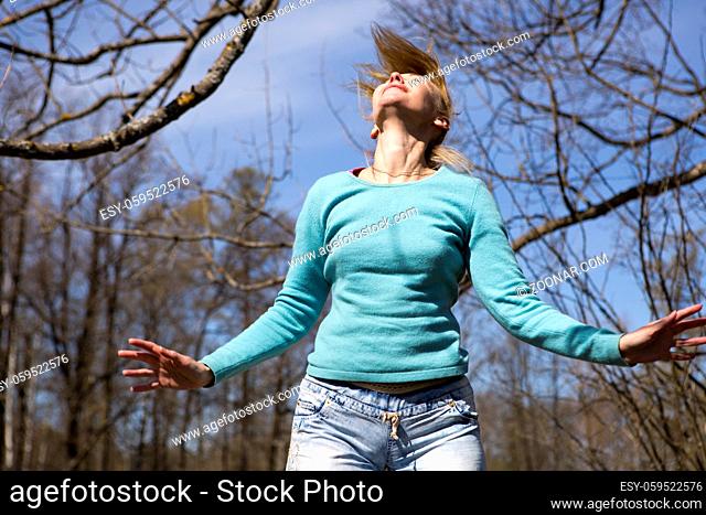 The happy young woman in bright clothes jumps in spring park