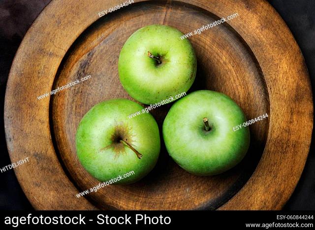 Three green apples in wooden plate