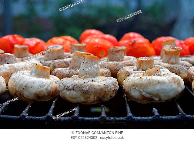 Vegetables in salt and spices being cooked on char grill, white champignons portobello mushrooms and red small tomatoes, close up, low angle view
