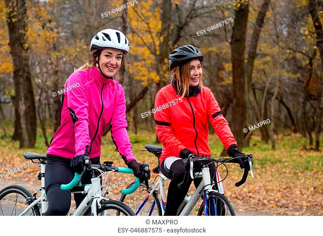 Two Young Smiling Female Cyclists with Road Bicycles Resting and in Park in Cold Autumn Day. Healthy Lifestyle
