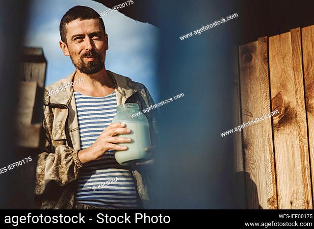 Mature man with glass jar of fresh milk on sunny day