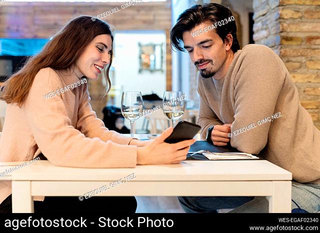 Young couple looking at smart phone while sitting in restaurant