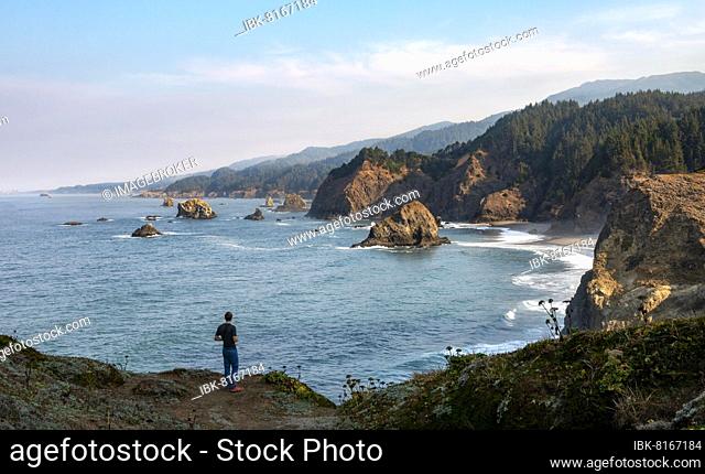 Young man standing on cliff, sandy beach and rocky coast, coastal landscape with rugged cliffs, Samuel H. Boardman State Scenic Corridor, Indian Sands Trail