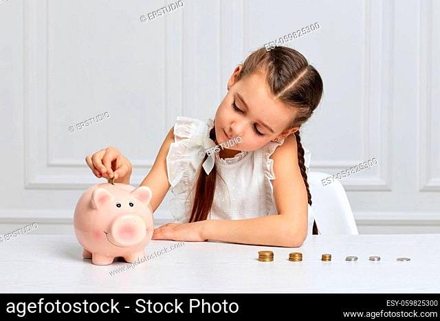 pretty little child girl putting a coin into pink piggy bank. kid saving money for future