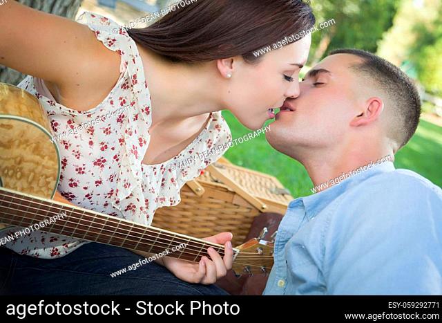 Affectionate Mixed Race Couple with Guitar Kissing in the Park