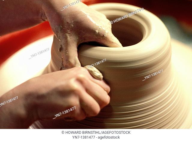 close up of a potter's hands as he carefully shapes his clay on the turning wheel