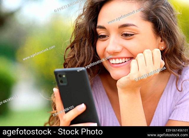 Happy woman checking smart phone smiling in a park