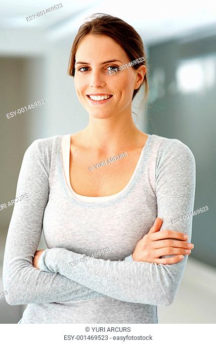 Portrait of relaxed beautiful young lady standing indoors with her hands folded