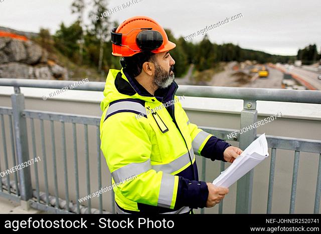 Male engineer in reflecting clothing holding blueprint