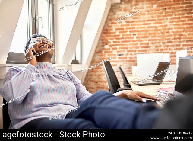 Laughing businesswoman looking up while talking on smart phone at office