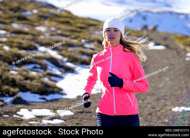 Young sportswoman running on mountain during winter on sunny day