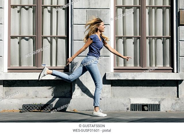 Netherlands, Maastricht, happy blond young woman running along building in the city