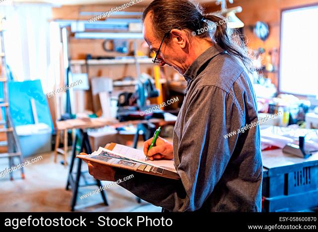 middle aged man with long hair wearing glasses in the garage with tools in the background. home inspector taking professional notes on his notebook