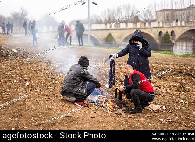 05 March 2020, Turkey, Edirne: Syrian refugees warm themselves at a small campfire in the Turkish border town of Edirne on the river ""Tunca Nehri"" near the...