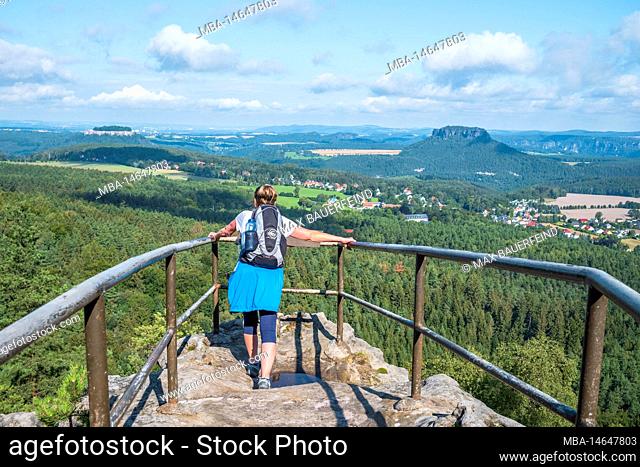 Senior woman hiking in the Elbe Sandstone Mountains with a view of the Papststein in the summer, Saxon Switzerland
