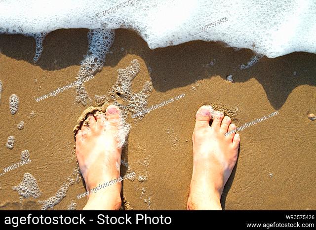Male feet standing on the beach watching the water waves from above