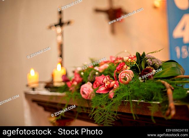 Interior of a Roman Catholic Church with polychrome decoration of the altar and flowers, with an out of focus cross with Jesus Christ in the background