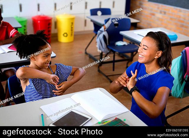 African american female teacher and a girl talking in hand sign language at elementary school