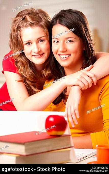 Two teenager girls hugging, smiling looking at camera