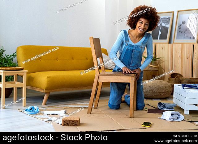 Redhead woman polishing wooden chair while kneeling on cardboard
