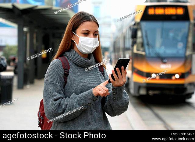 Young woman with protective mask buying and paying for online transport ticket via banking application on smartphone in city street