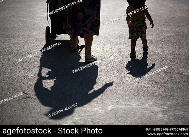 SYMBOL - 16 July 2023, Berlin: The shadows of a mother pushing a stroller and walking next to her toddler can be seen against the light