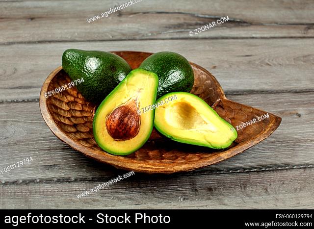 Avocados in wooden carved bowl, one of them cut in half, seed visible