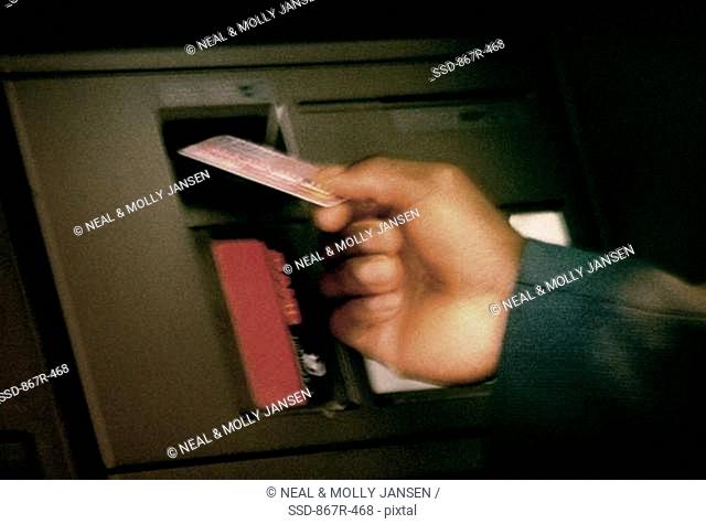 Close-up of a person's hand holding an ATM card in front of an ATM