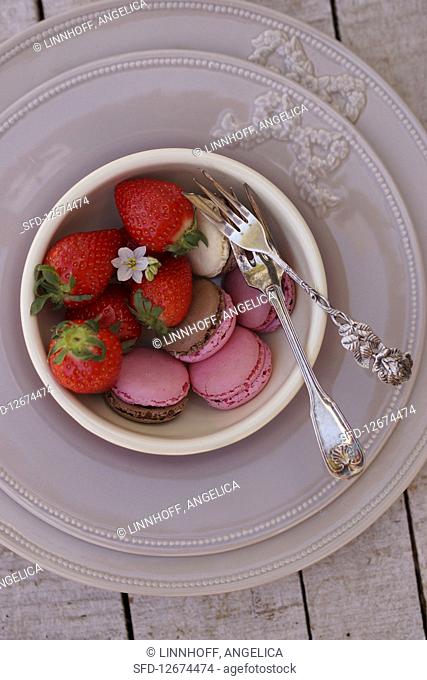 Various macarons and fresh strawberries in small bowls on a place setting