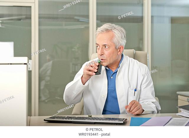 Doctor at desk drinking liquor secretly