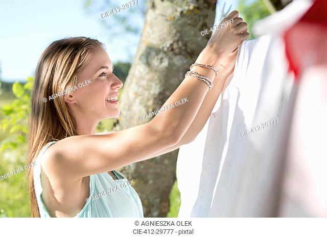 Smiling young woman hanging laundry on clothesline