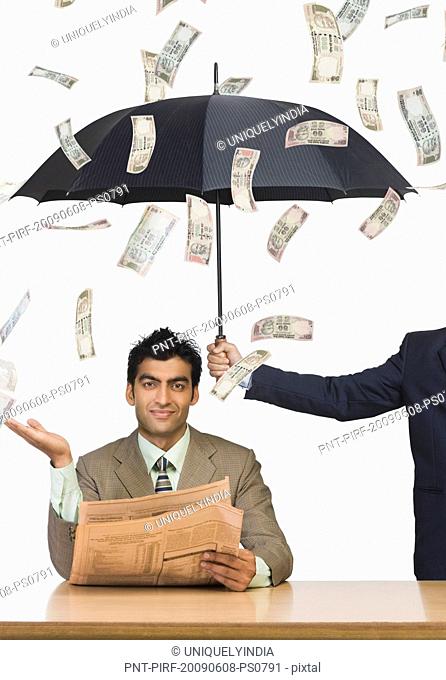 Money falling on businessman sitting under an umbrella